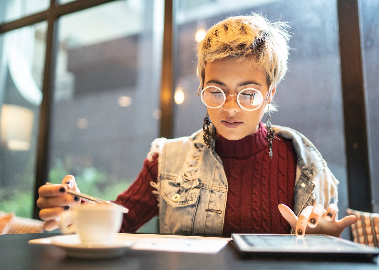 Young woman looking at digital investments on a tablet in cafe